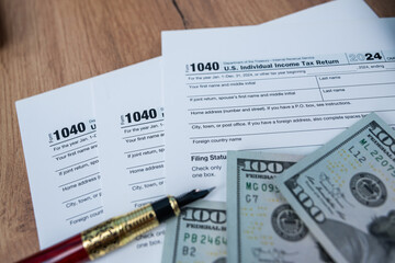 Fototapeta premium Income tax form with fountain pen and dollar cash on wooden table background