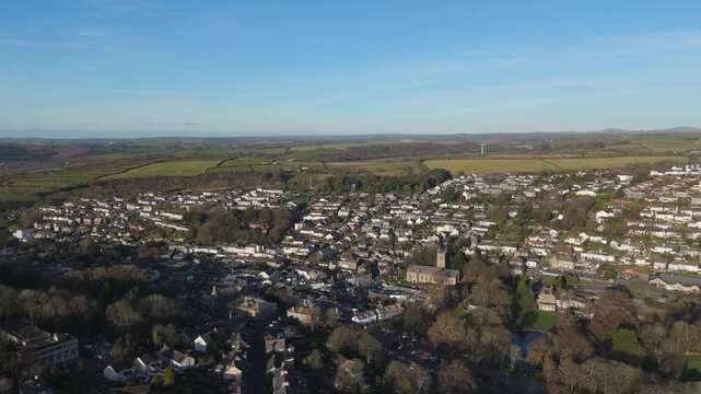 Aerial view of a town featuring a church and houses with a backdrop of green fields and clear blue skies, Bodmin, United Kingdom.