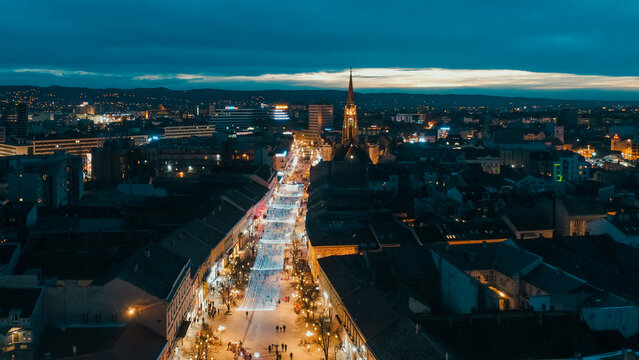 Aerial view of the bright pedestrian street cutting through the dark landscape, with the church tower reaching for the fading light, Novi Sad, Serbia.
