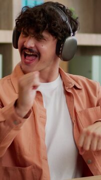 Relaxed Caucasian businessman using mobile phone listening music in headphones dancing business man male guy manager with smartphone wearing earphones dance listen audio funny move at office table