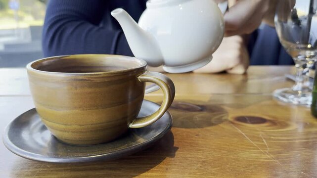 A man pours tea from a teapot into a cup. Tea drinking in a cafe. Steaming tea in a cup.