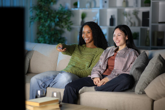 Diverse happy couple watching tv in the night at home