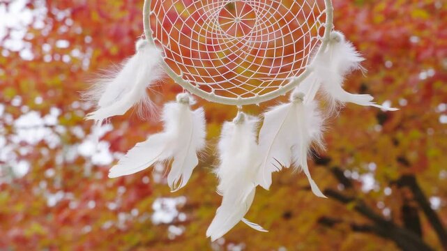 Dreamcatcher swaying gently in the autumn breeze against a backdrop of vibrant fall foliage. Symbolizes protection, dreams, and nature's beauty