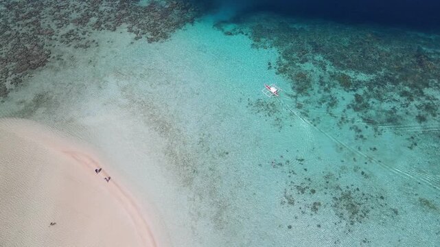 Aerial view of a boat navigating through the turquoise waters near a white sandy beach, contrasting with the deep blue sea, Coron, Mimaropa, Philippines.