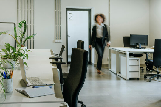 Businesswoman walking through modern office interior with desk and plants