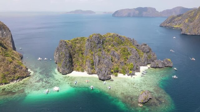 Aerial view of boats dotting the turquoise waters around the dramatic karst islands featuring rocky cliffs and hidden beaches, El Nido, Mimaropa, Philippines.