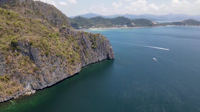 Aerial view of rocky islands meeting the turquoise sea, where boats leave trails on the water, creating a mesmerizing contrast of nature's beauty, El Nido, Mimaropa, Philippines.