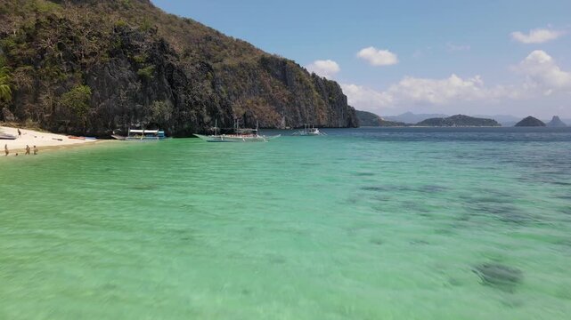 Aerial view of boats floating over turquoise waters near jagged cliffs, a serene coastal scene showcasing the natural beauty, El Nido, Mimaropa, Philippines.