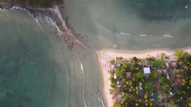 Aerial view of a pristine beach meeting the turquoise sea, with boats resting on the shore, framed by lush greenery, El Nido, Mimaropa, Philippines.