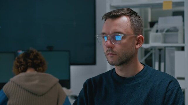 Focused diverse software engineers and AI developers working on programming code on computer screens in a dark office. Concept of machine learning, digital transformation, and future technology.