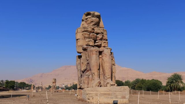 Colossi of Memnon pair of royal statues in archaeological zone Luxor Egypt, impressive pharaonic monuments with palm oasis and desert valley panoramic view