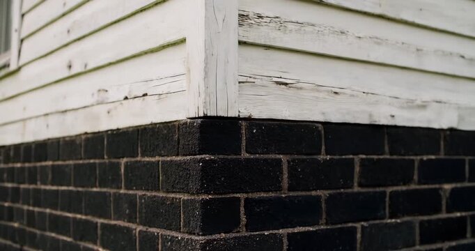Close-up of weathered house exterior with white siding and black brick foundation