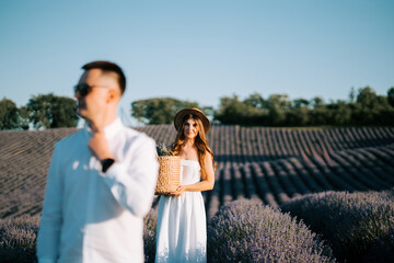 Naklejka premium Couple walks through lavender field at sunset carrying a basket and enjoying their time together