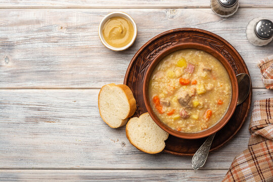 Soup kulesh with millet, potatoes, onion, carrot, meat and bacon in ceramic bowl on wooden background.