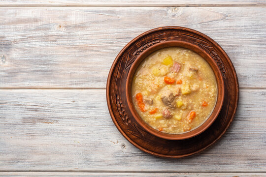 Soup kulesh with millet, potatoes, onion, carrot, meat and bacon in ceramic bowl on wooden background.