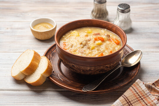 Soup kulesh with millet, potatoes, onion, carrot, meat and bacon in ceramic bowl on wooden background.