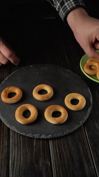Making doughnuts or Bubliki by hand on a wooden table with a plate nearby in a well-lit kitchen setting