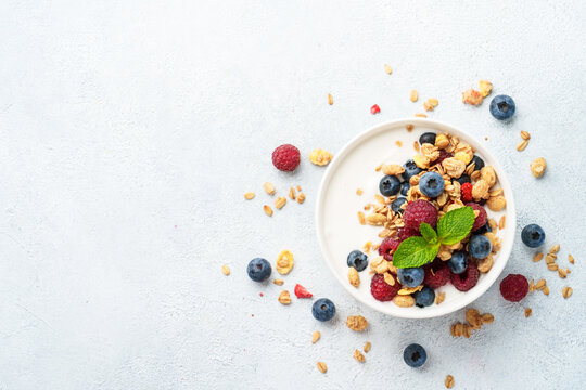 Yogurt with fresh berries and granola on white table.