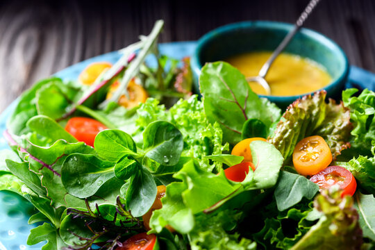 Mixed salad greens with cherry tomatoes and dressing on wooden table, fresh lettuce mix. Natural food styling