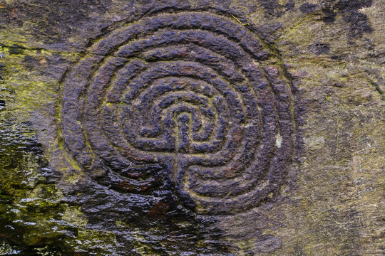 View of an ancient labyrinth carved into a moss-covered stone, its weathered surface hinting at centuries of mystery and contemplation, Cornwall, England, United Kingdom.