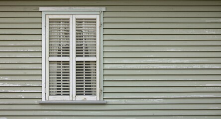 Shuttered double hung window with white wooden trim on a green vintage horizontal clapboard wall