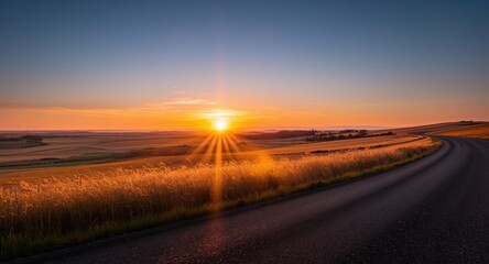 Radiant sunset skyline over a winding road and expansive tall grass fields