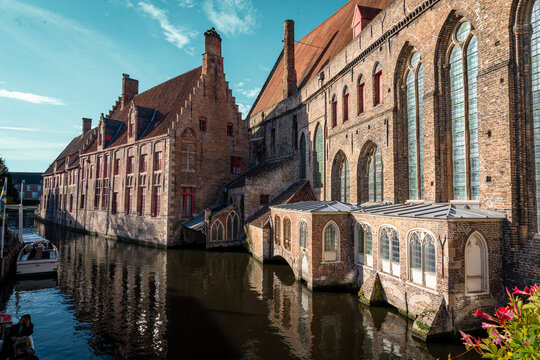 Landscape shot of buildings over canal river from bridge in bruges in belgium with orange gothic details on the stone and cloudy clear blue skies above in autumn