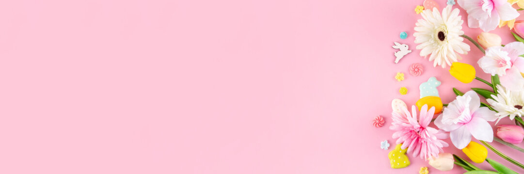 Beautiful spring flowers bouquet with Easter decorations on pink background. Easter holiday flat lay with eggs, rabbits and springtime flowers. Greeting card background with copy space