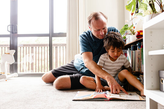 Boy reading book with dad at home on the floor
