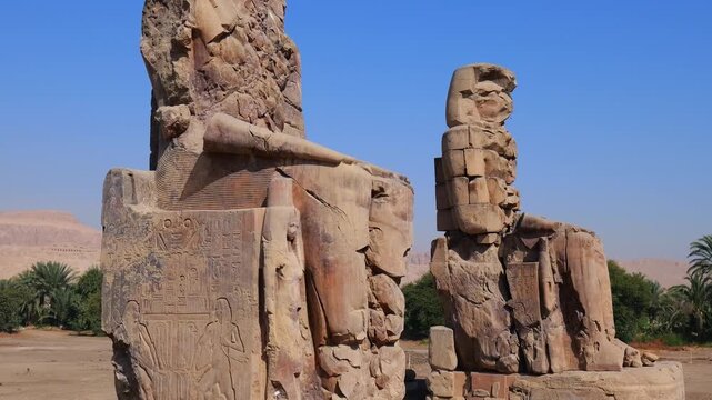 Massive stone statues of Amenhotep III at Colossi of Memnon site in Luxor with mountain backdrop, weathered sandstone pharaonic sculptures and heritage landmark