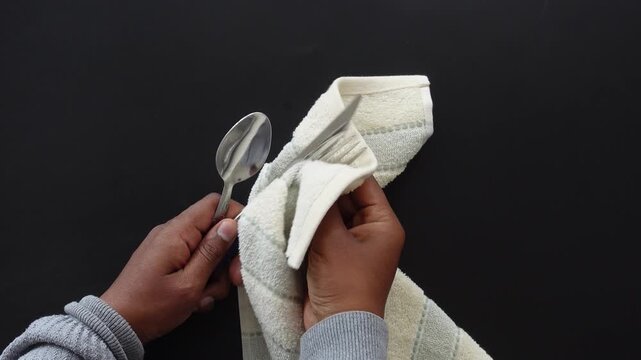 Close up of person hands polishing and cleaning silverware with a white cloth against a black background