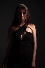 Naklejka premium Woman posing in elegant black dress with cutout detail, capturing beauty, fashion, and mysterious mood through low-key studio lighting