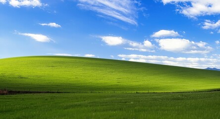 Fototapeta premium Vibrant hillside panorama with fresh green grass covering rolling hills beneath a bright sky with soft clouds