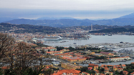Fototapeta premium Wide coastal cityscape with bay, cruise liner, marina and container terminal, backed by mountains. Travel, shipping and logistics concept.