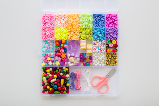 Case with colorful plastic parts, scissors, elastic strings. Light gray table background. Set for little child girl bracelet and necklaces making. Creating beaded jewellery. Flat lay. Top down view.