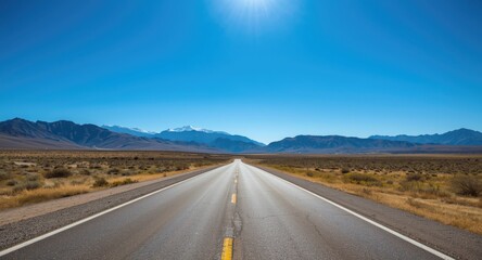 Clear blue sky illuminating a straight asphalt road with mountain vistas
