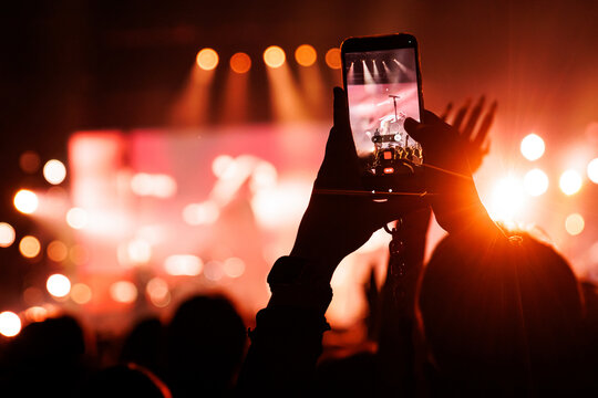 Close up of smartphone recording live band in red concert light