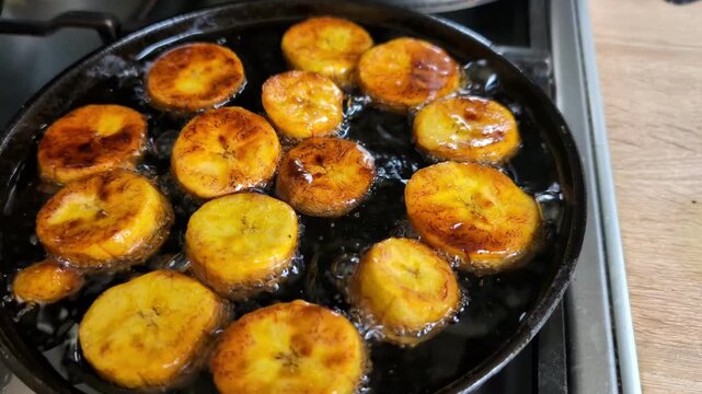 Making patacones or kelewele: Yellow plantain fruit being fried on a cast iron black pan