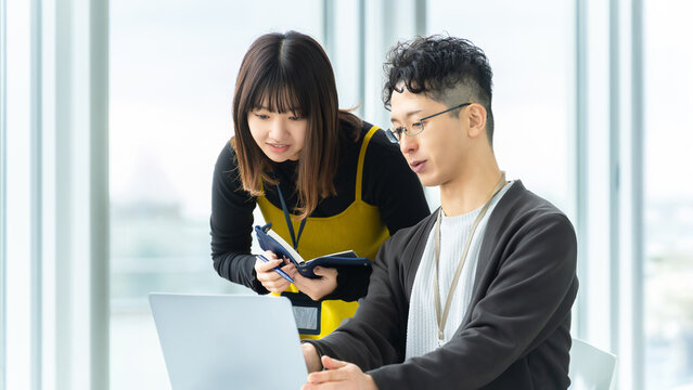 ノートパソコンを見ながら相談する新人社員と先輩社員, New employee consulting with senior colleague while looking at laptop
