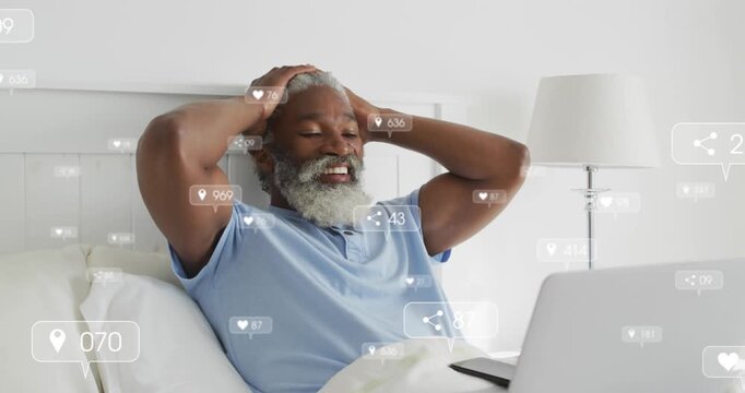 Animation of social media icons on african american man having a video call on laptop in bed at home