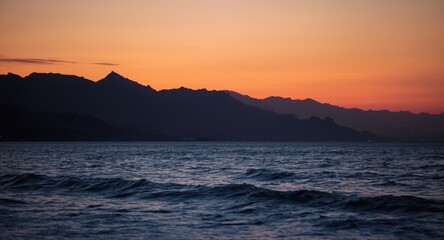 Twilight ocean scene with dark mountain outlines under warm glowing sky