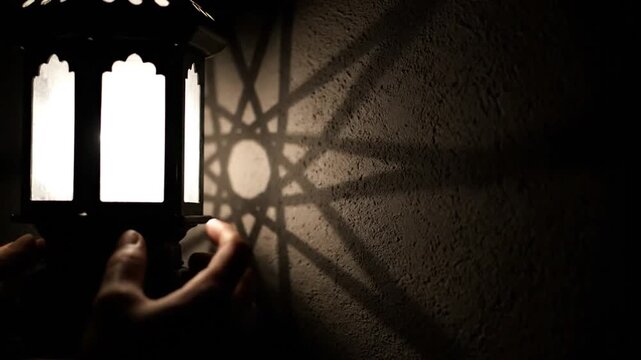 Shadows cast by a lantern create an intricate star pattern on a textured wall in a dimly lit room