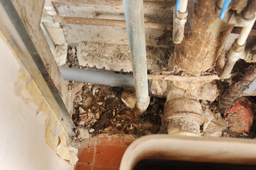 Old rusty plumbing pipes and debris in a basement during repair.