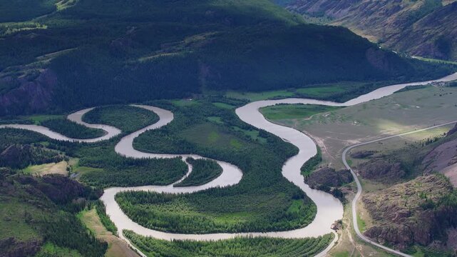 Slow aerial flyover of winding meandering river through remote green Altai mountain valley showing progressive turns.
