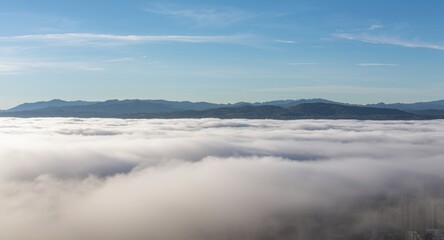 Obraz premium Low cloud blanket covers urban area with mountain vistas visible far away beneath a bright sky