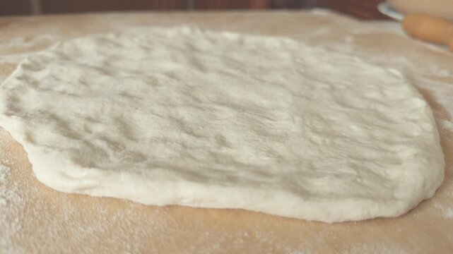 Rotating view of a raw pizza dough or focaccia on a wooden surface, close-up.