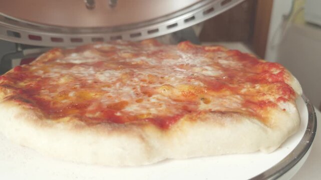 Opening lid of round pizza oven revealing cooked pizza with slight rotation.