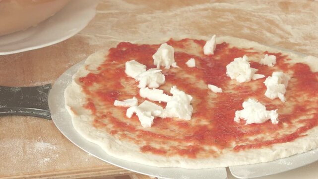 Adding mozzarella cheese to a pizza with tomato sauce on a pizza peel, in close-up.