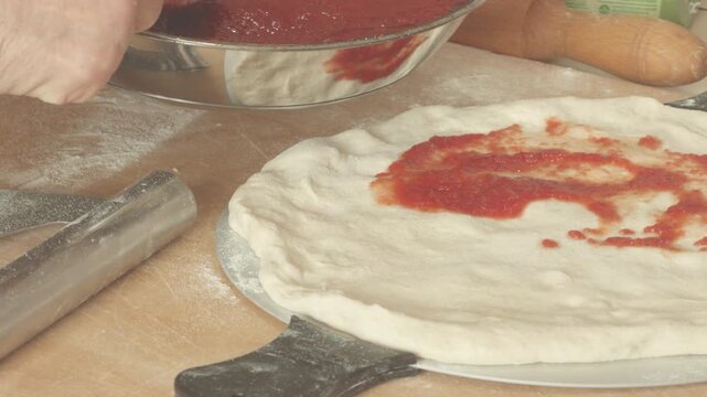 Spreading tomato sauce on a pizza dough, close-up, preparation.