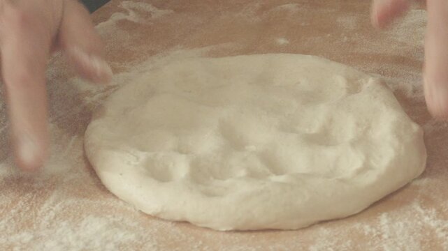 A woman shaping pizza dough with her hands, in a close-up, front view.